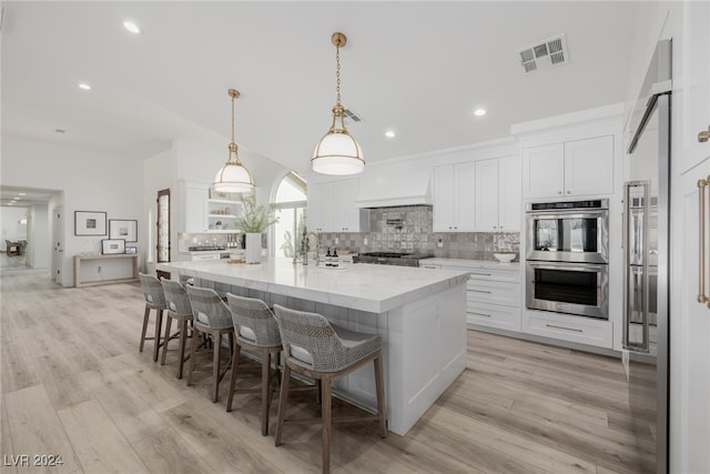 kitchen featuring appliances with stainless steel finishes, a spacious island, light hardwood / wood-style floors, decorative light fixtures, and white cabinets