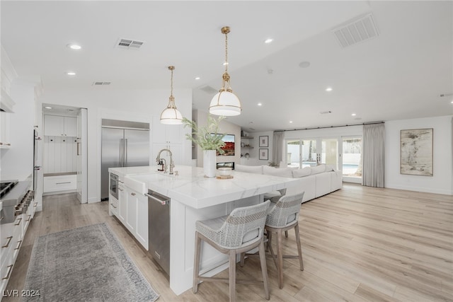 kitchen with a spacious island, light hardwood / wood-style flooring, vaulted ceiling, decorative light fixtures, and white cabinets