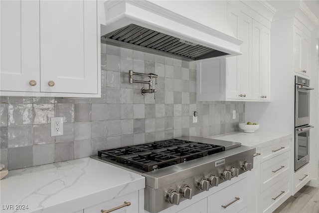 kitchen featuring appliances with stainless steel finishes, white cabinetry, light hardwood / wood-style floors, custom range hood, and light stone counters