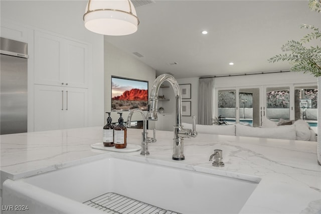 kitchen featuring sink, light stone counters, vaulted ceiling, and stainless steel built in refrigerator