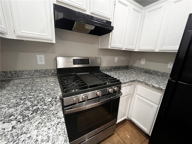 kitchen featuring white cabinetry, stainless steel gas range oven, light stone countertops, and black fridge