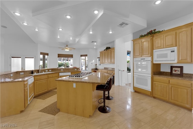 kitchen with light stone counters, a kitchen island, a kitchen breakfast bar, sink, and white appliances