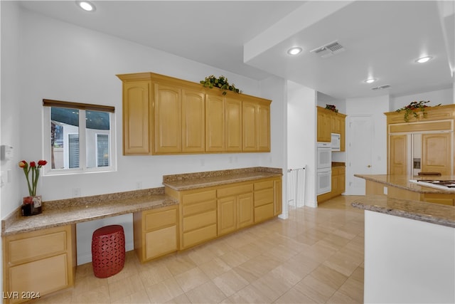 kitchen featuring light brown cabinets, paneled fridge, light stone countertops, and built in desk