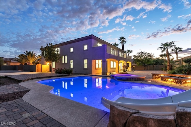 pool at dusk featuring a patio area and an in ground hot tub