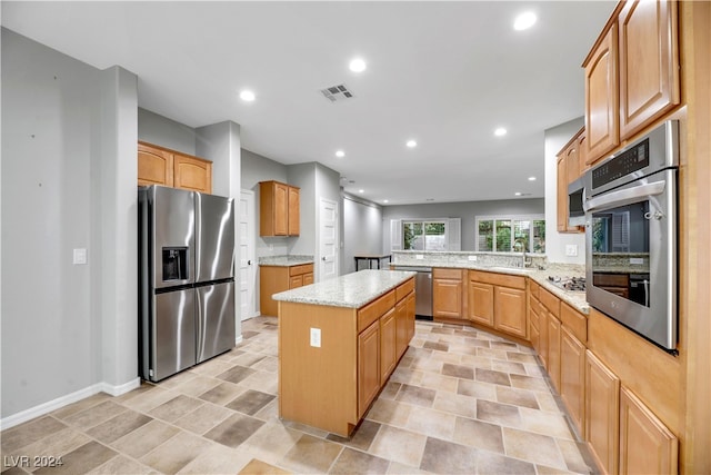 kitchen with sink, a kitchen island, kitchen peninsula, stainless steel appliances, and light stone counters