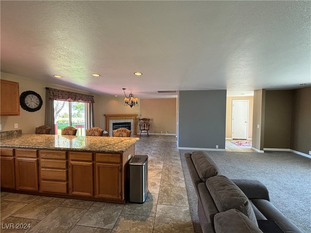 kitchen with kitchen peninsula, a tile fireplace, decorative light fixtures, light colored carpet, and a textured ceiling