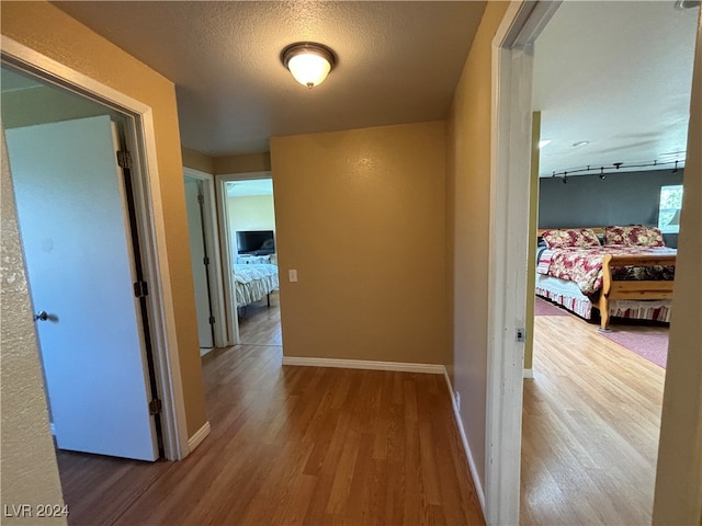 hall with a textured ceiling, hardwood / wood-style flooring, and track lighting