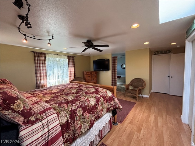 bedroom featuring track lighting, ceiling fan, light wood-type flooring, a textured ceiling, and a skylight