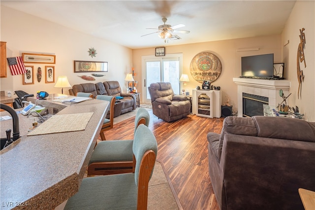 living room with an AC wall unit, hardwood / wood-style flooring, a tile fireplace, and ceiling fan