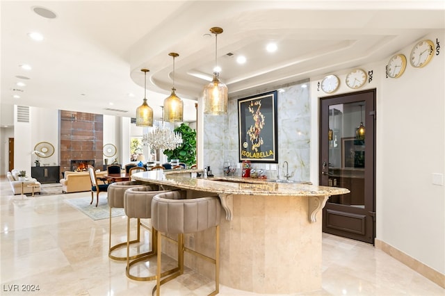 bar with light stone countertops, a fireplace, decorative light fixtures, and a tray ceiling