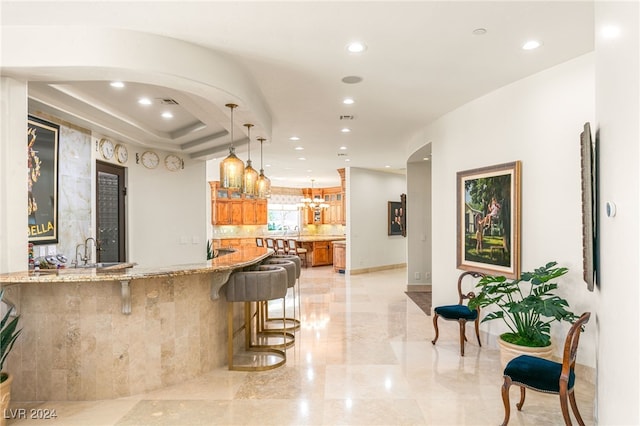 kitchen with light stone countertops, sink, kitchen peninsula, decorative light fixtures, and a breakfast bar