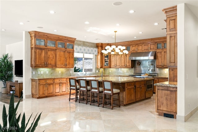 kitchen with decorative backsplash, an island with sink, a kitchen breakfast bar, pendant lighting, and light stone counters