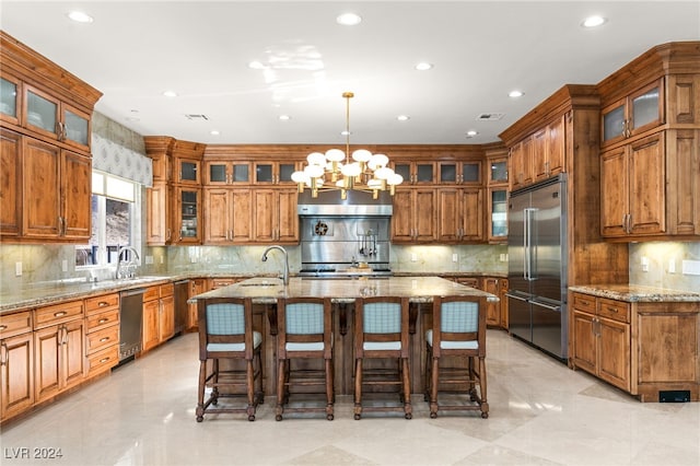 kitchen featuring a kitchen island with sink, built in fridge, a breakfast bar, decorative light fixtures, and a chandelier