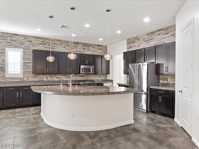 kitchen with appliances with stainless steel finishes, hanging light fixtures, dark brown cabinets, and an island with sink