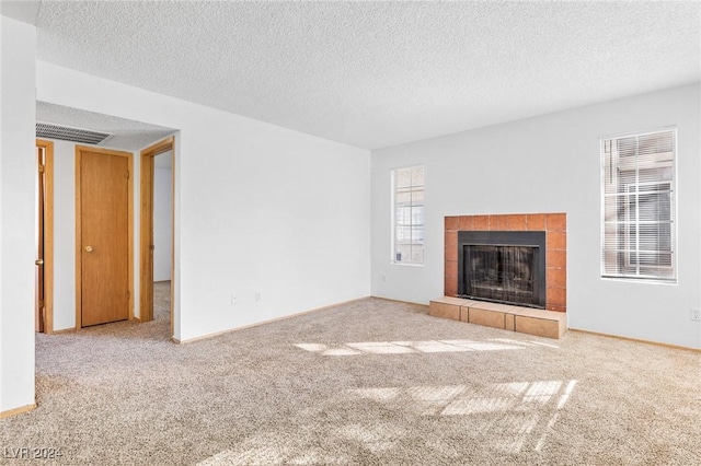 unfurnished living room with baseboards, visible vents, carpet, a textured ceiling, and a fireplace