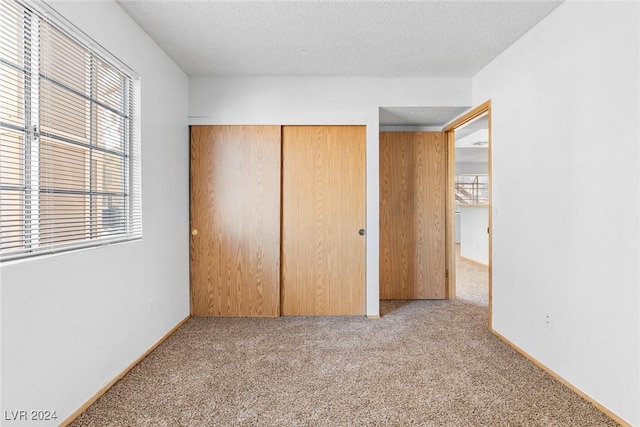 unfurnished bedroom with a textured ceiling, baseboards, a closet, and light colored carpet