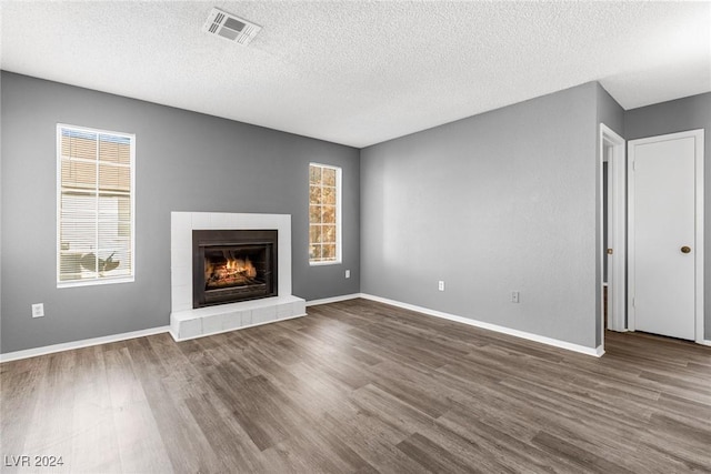 unfurnished living room featuring dark wood-style floors, a tile fireplace, visible vents, and baseboards