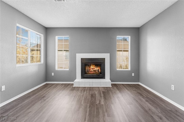 unfurnished living room featuring a textured ceiling, dark wood-style flooring, a tiled fireplace, and baseboards