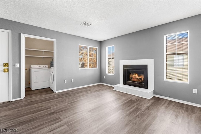 unfurnished living room with visible vents, dark wood-type flooring, washing machine and dryer, a textured ceiling, and a tile fireplace