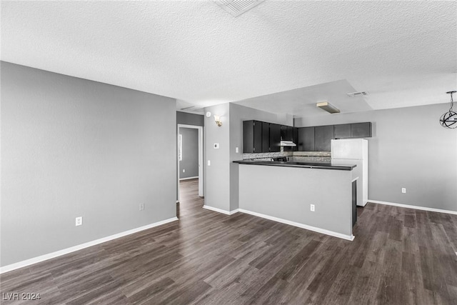 kitchen featuring visible vents, dark countertops, dark wood-type flooring, freestanding refrigerator, and a peninsula