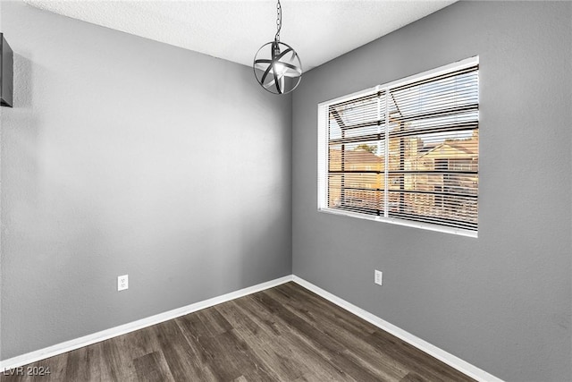 spare room featuring an inviting chandelier, a textured ceiling, baseboards, and dark wood-type flooring