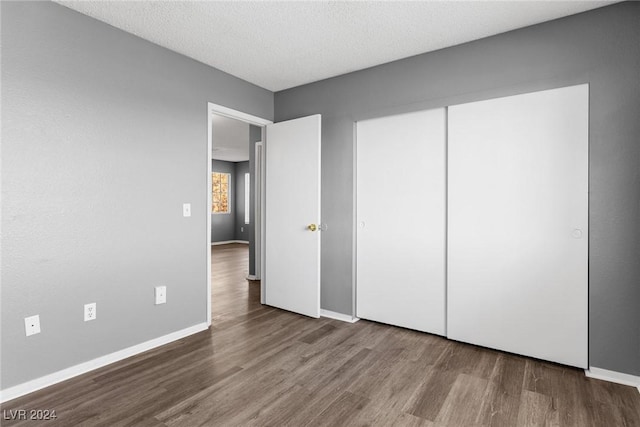 unfurnished bedroom featuring a textured ceiling, a closet, wood finished floors, and baseboards