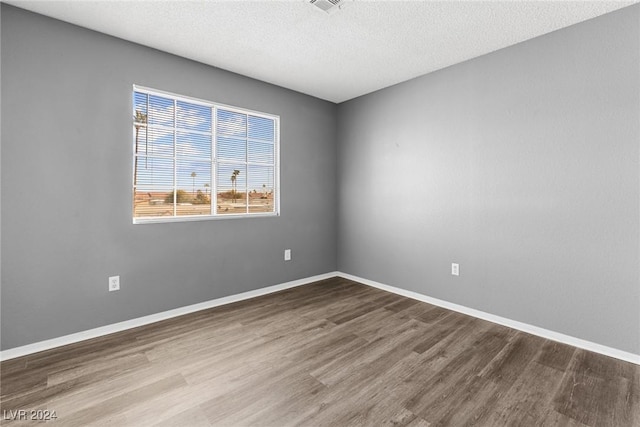 empty room with a textured ceiling, wood finished floors, visible vents, and baseboards