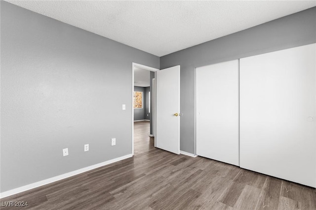 unfurnished bedroom with a closet, a textured ceiling, baseboards, and wood finished floors