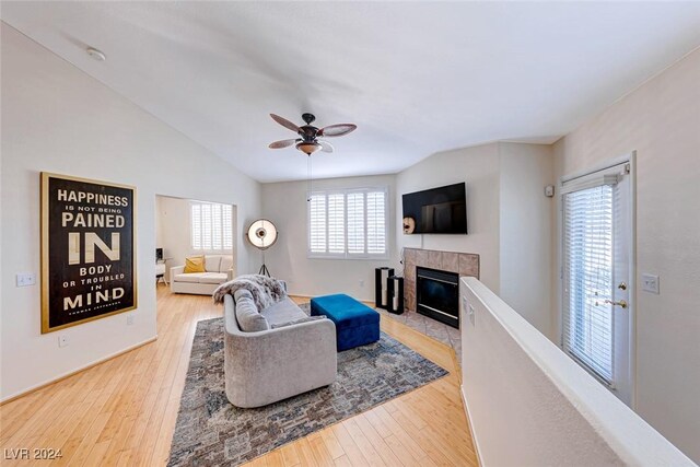 living room with ceiling fan, lofted ceiling, wood-type flooring, and a tiled fireplace