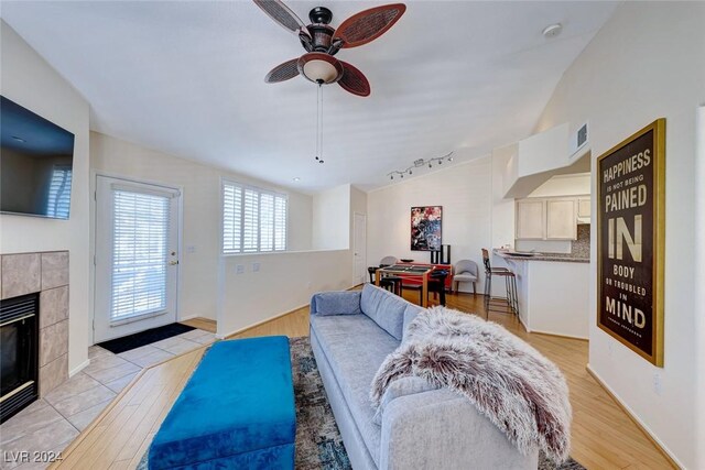 living room with ceiling fan, a fireplace, light hardwood / wood-style floors, and vaulted ceiling