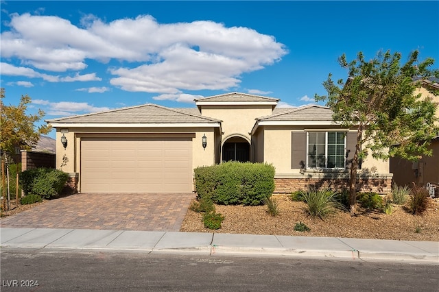 view of front of home featuring an attached garage, stone siding, decorative driveway, and stucco siding