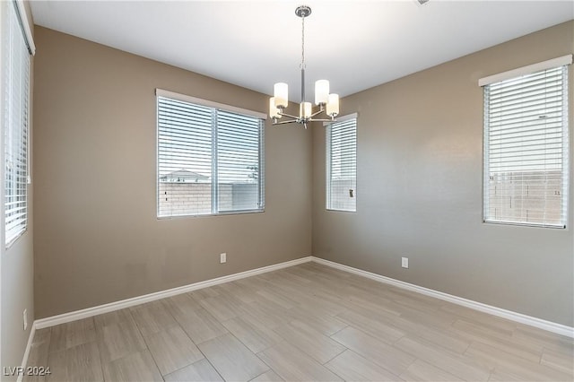 spare room featuring an inviting chandelier, light wood-style flooring, and baseboards