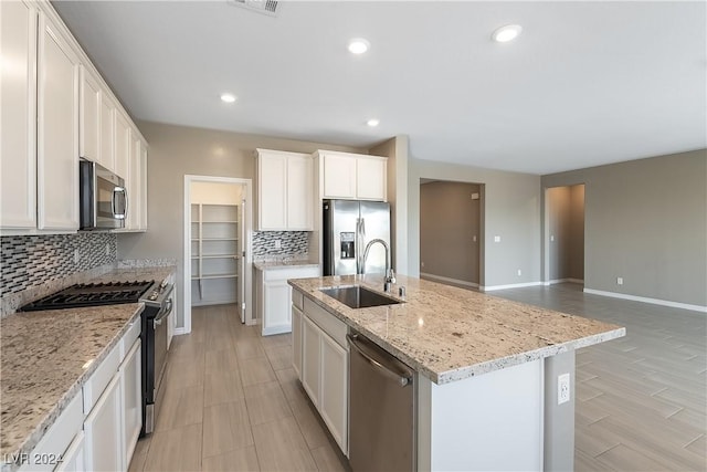 kitchen with a center island with sink, light stone counters, stainless steel appliances, white cabinetry, and a sink