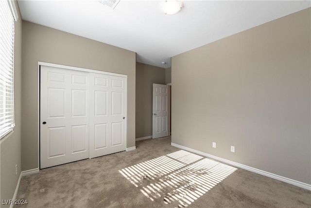 unfurnished bedroom with a closet, light colored carpet, visible vents, and baseboards