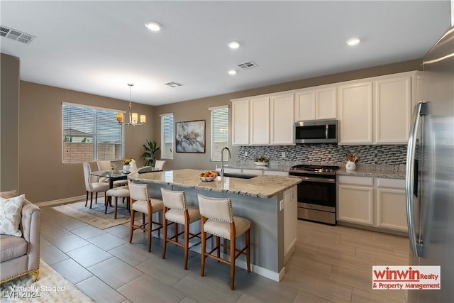 kitchen with a center island with sink, stainless steel appliances, hanging light fixtures, white cabinets, and a sink