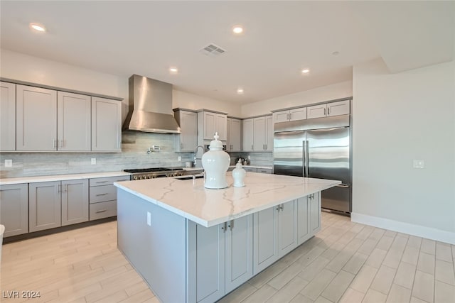 kitchen featuring wall chimney range hood, a center island, stainless steel appliances, light stone counters, and decorative backsplash