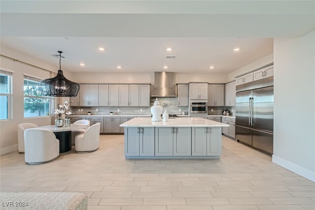 kitchen with a kitchen island with sink, wall chimney range hood, stainless steel appliances, pendant lighting, and tasteful backsplash