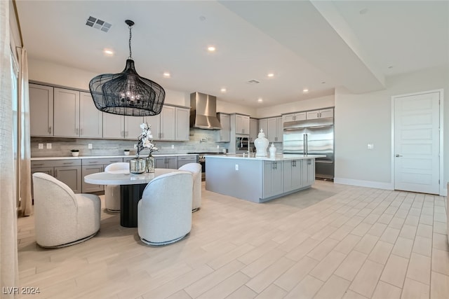 kitchen with tasteful backsplash, appliances with stainless steel finishes, wall chimney exhaust hood, pendant lighting, and a center island with sink