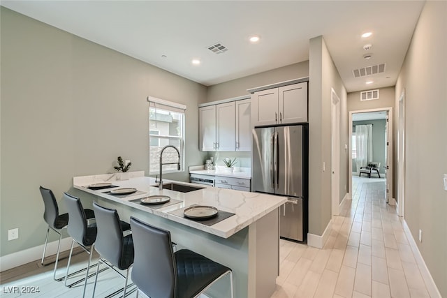 kitchen with kitchen peninsula, stainless steel fridge, a kitchen bar, gray cabinets, and sink