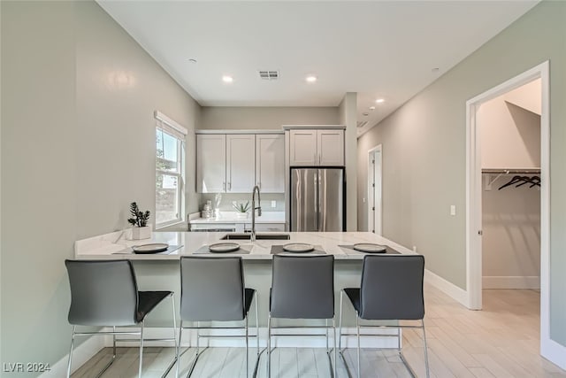 kitchen with kitchen peninsula, stainless steel fridge, a breakfast bar, light wood-type flooring, and sink