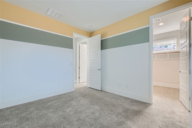 unfurnished bedroom with a walk in closet, a closet, and carpet flooring