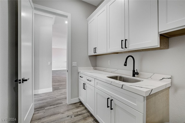 kitchen with light hardwood / wood-style flooring, white cabinets, light stone counters, and sink