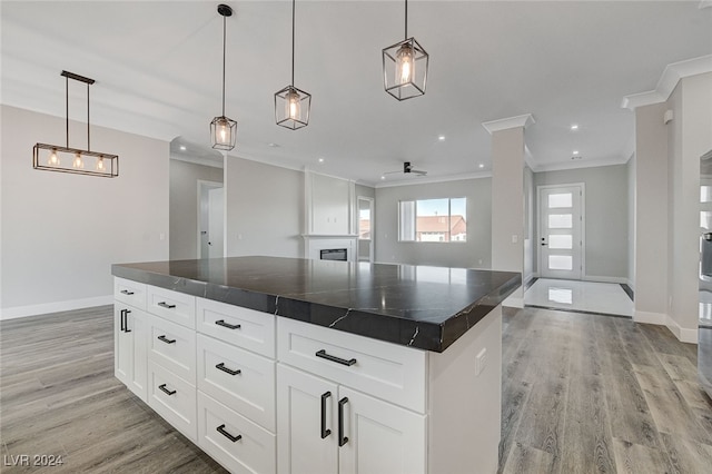 kitchen with white cabinets, a kitchen island, light wood-type flooring, ornamental molding, and pendant lighting