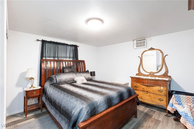 bedroom featuring a textured ceiling, dark hardwood / wood-style flooring, and a wall mounted air conditioner