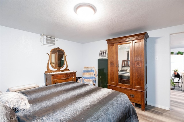 bedroom featuring light hardwood / wood-style flooring, a textured ceiling, and a wall mounted AC