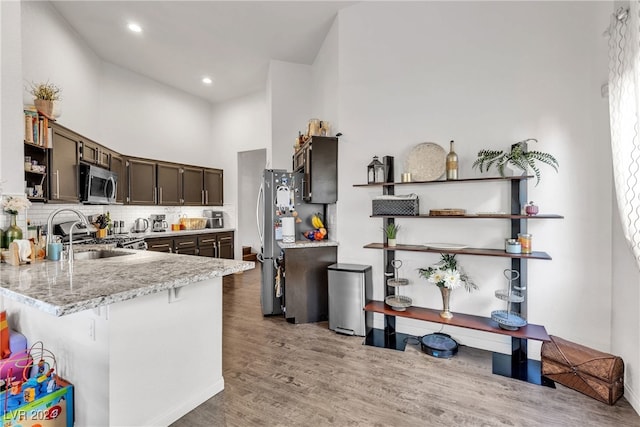 kitchen with sink, stainless steel appliances, a high ceiling, dark brown cabinets, and light wood-type flooring