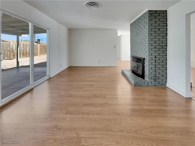 unfurnished living room with light wood-type flooring and a brick fireplace