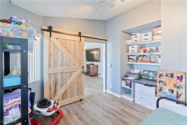 bedroom featuring vaulted ceiling, a barn door, light wood-type flooring, and ceiling fan