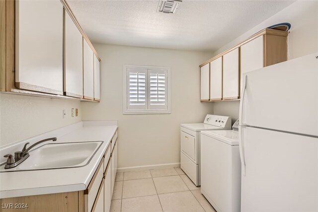 clothes washing area with sink, light tile patterned flooring, separate washer and dryer, a textured ceiling, and cabinets