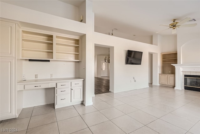 kitchen featuring built in desk, ceiling fan, light tile patterned floors, high vaulted ceiling, and a fireplace